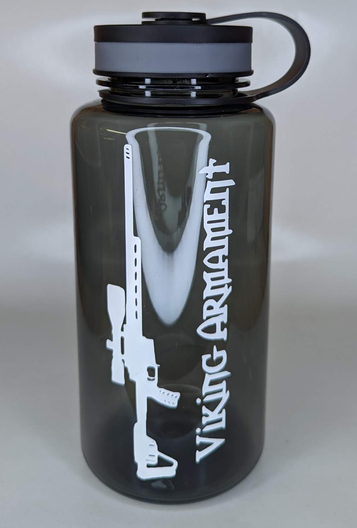 VA 32oz Water Bottle Durable | Leak-Resistant | Everyday Ready The Water Bottle is built to keep up with your daily grind, backcountry adventures, and range days alike. Crafted from tough, BPA-free plastic, this bottle is designed to handle impact and resist wear no matter where your mission takes you. The wide-mouth opening makes it easy to fill, clean, and mix in your favorite hydration additives. With a leak-resistant screw-on lid and durable loop-top design, it’s perfect for tossing into your pack or clipping to your gear with confidence. The slim profile fits most backpack pockets and cup holders, making it a reliable companion whether you’re chasing elevation or punching paper at the range. Finished in a smoked translucent color with the Viking Armament logo, it’s a subtle nod to those who live the forged life—on the move, with purpose. Components: BPA-free durable plastic bottle Wide-mouth design for easy filling and cleaning Leak-resistant screw-on lid Integrated carry loop Smoked translucent finish with Viking Armament branding Notes: Not designed for hot liquids Hand wash recommended to preserve graphics Fits most standard-size backpack bottle pockets Stay hydrated with a bottle that’s built for battle-tested days and backwoods treks. The VA Water Bottle is the no-fuss, field-proven essential for warriors who carry their gear with purpose.